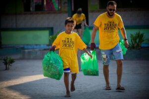 a man and a boy carrying trash bags wearing trash hero t-shirts